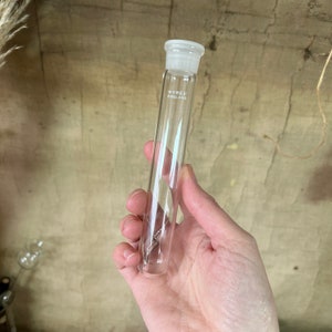 May include: A clear glass test tube with a white plastic stopper. The tube is labelled "PYREX ENGLAND".