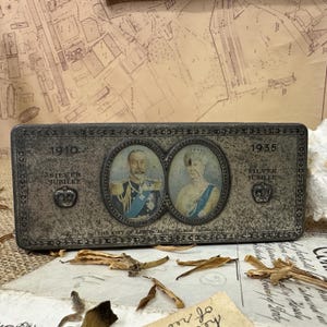 May include: A silver metal box featuring portraits of King George V and Queen Mary. The box commemorates the 1910 and 1935 Silver Jubilees of the British monarchy. The inscription on the box reads "1910 Silver Jubilee" and "1935 Silver Jubilee".