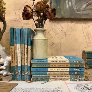 May include: A stack of vintage blue paperback books with a pelican illustration on the cover. The books are titled "Totem and Taboo", "The Centuries Poetry", "More Common Wild Flowers", "Common Wild Flowers", "Juvenile Delinquency", "Lives of the Great Composers Vol. 2", "Music in England", "The Personality of Man", "Common Wild Flowers", "More Common Wild Flowers", "Adventures of Ideas", "The Centuries Poetry", "Sigmund Freud", "Hood to Hardy", "2. Hutchinson", "3. Hutchinson", "A. E. Jones", "A Bacharach", "Oh", "More Common Wild Flowers", "Nosnihin", "Common Wild Flowers", "1. Hutchinson", "G. N. M. Tyrrell", "Eric Blon", "The Century's Poetry (21".