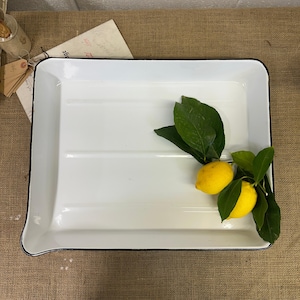 May include: White enamel rectangular serving tray with a black rim. Two lemons with green leaves are on the tray.