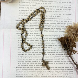 May include: A vintage rosary with brown and white beads and a metal cross pendant. The rosary is lying on a page of a legal document with text about a mortgage.