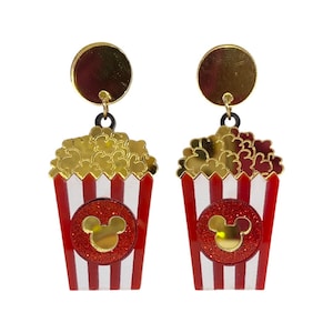 Puede incluir: Pendientes novedosos con forma de cubos de palomitas de ma&iacute;z. Los pendientes tienen un dise&ntilde;o de cubo a rayas rojas y blancas con una cabeza de Mickey Mouse dorada en un c&iacute;rculo de purpurina roja. Las palomitas son doradas y la parte superior es un c&iacute;rculo dorado.