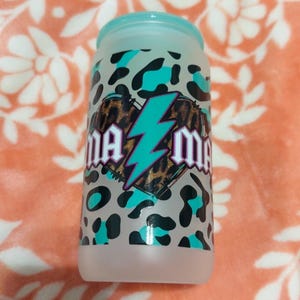 May include: A frosted glass tumbler with a teal lid and a leopard print design. The tumbler features the text "Mama" with a teal lightning bolt and leopard print heart.
