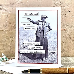 May include: A humorous greeting card with a vintage photo of a woman holding a gun. The text reads "My wife said that she missed me. Normally, that's a good thing, but now she's reloading."