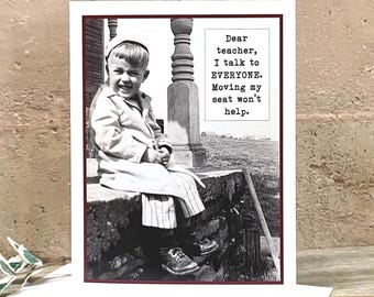 May include: A greeting card featuring a black and white vintage photograph of a young child sitting on a porch, with the text: Dear teacher, I talk to EVERYONE. Moving my seat won't help. The card is displayed with a wooden fountain pen on a white envelope.