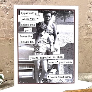 May include: A humorous greeting card with a black and white photo of a woman and her two children. The text on the card reads "Apparently, when you're asked who your favorite child is, you're expected to pick one of your own. I know that now."