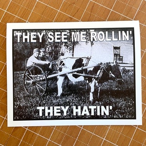 May include: A black and white image of two people riding in a horse drawn cart. The image is printed on a white background with the text 