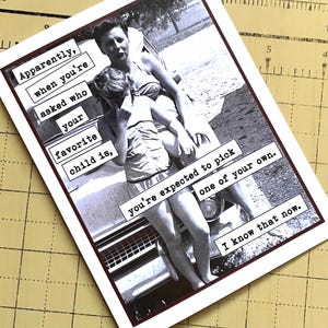 May include: A black and white photo of a woman holding a young girl in her arms. The photo is on a card with the text "Apparently, when you're asked who your favorite child is, you're expected to pick one of your own. I know that now."