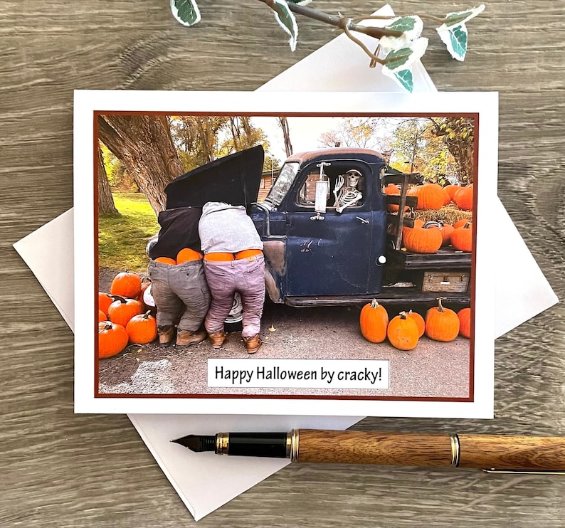 May include: Halloween greeting card featuring a humorous scene with two people working on a vintage blue truck, a skeleton in the driver's seat, and pumpkins. The card reads "Happy Halloween by cracky!"
