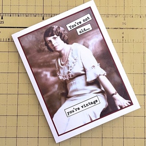 May include: A vintage-style greeting card with a sepia-toned photo of a woman in a white dress. The text on the card reads "You're not old... you're vintage."