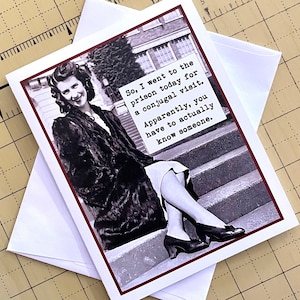 Pu&ograve; includere: Un biglietto d'auguri divertente con una foto in bianco e nero di una donna con un cappotto di pelliccia seduta su una scala. Il testo sulla carta dice: "Quindi, sono andata in prigione oggi per una visita coniugale. A quanto pare, devi davvero conoscere qualcuno."