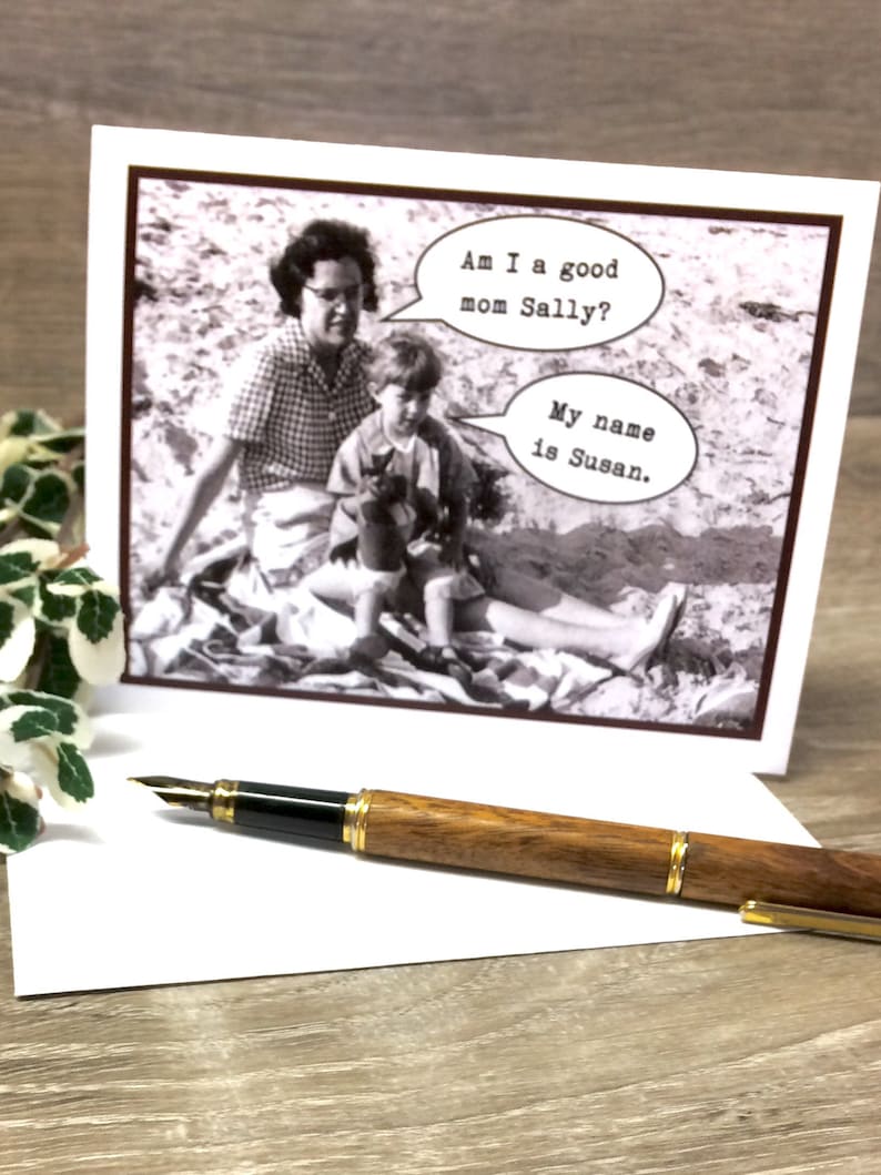 Puede incluir: Una tarjeta de felicitaci&oacute;n con una foto en blanco y negro vintage de una madre y un ni&ntilde;o, con bocadillos de di&aacute;logo. El texto dice: "Am I a good mom Sally?" y "My name is Susan." Una pluma estilogr&aacute;fica de madera con detalles dorados descansa sobre la tarjeta.