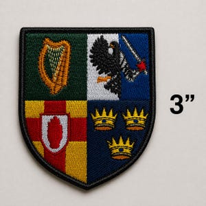 May include: Embroidered patch featuring a heraldic shield design. The shield is divided into four quadrants with various symbols: a harp, an eagle, a sword, and three crowns. The patch measures 3 inches (7.6 cm) in height.