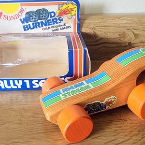Puede incluir: Coche de carreras de juguete de madera con ruedas naranjas y una pegatina "Mean Streak". El coche forma parte de la serie "Wood Burners", con su caja original visible. La caja presenta el texto "Rally 1 Set".