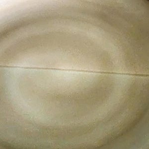 Op de afbeelding: Een grote, ronde keramische plaat met een lichtbruin, wervelend ontwerp. De plaat heeft een donkerbruine rand en een subtiele lijn die het midden in tweeën deelt. De plaat is geschikt voor het serveren van voedsel.