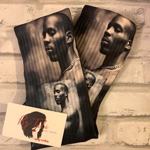 May include: Black and white printed fabric featuring a portrait of a man wearing a chain necklace. The fabric is folded, with the image repeated on each side. A business card with the text "By Tabi Event Designs" is also present.