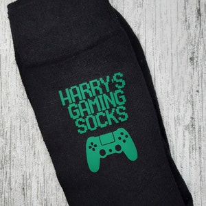 May include: Black socks with a green video game controller and the text "HARRY'S GAMING SOCKS" in a pixelated font.