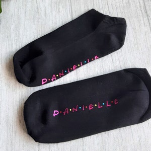 May include: Two black ankle socks with the name "D.A.N.I.E.L.L.E" written in pink, blue, and yellow letters on the bottom of each sock.