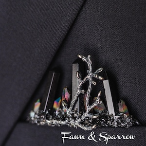 May include: A black crystal and silver branch pin with the text "Faun & Sparrow" on a black suit jacket.