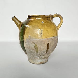 May include: A white ceramic mug with a black handle and the text "But First, Coffee" in a black, handwritten-style font. The mug is on a white surface.