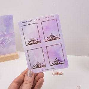May include: A sheet of four purple and white watercolour sticker frames with a gold foil design. The sticker sheet says "Fancy Frames - Purple" and "Sticker Sheet | D-55".