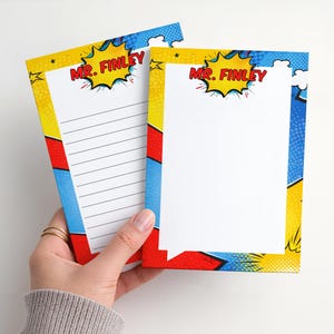 May include: Two comic book-style notepads with a white interior and a colorful border. The border features red, yellow, and blue panels with the text "MR. FINLEY" in a yellow speech bubble. One notepad has lined pages.