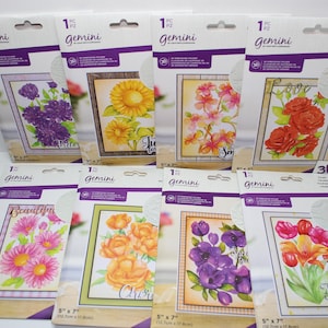 May include: A collection of Gemini 3D die-cutting and embossing folders featuring floral designs. Each package displays a different flower arrangement, including roses, sunflowers, and tulips. The packages are 5" x 7" (12.7cm x 17.8cm) and include the text "Gemini".