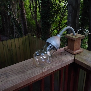 May include: A vintage-style outdoor light fixture with a clear glass globe and a metal base, mounted on a wooden post on a deck.