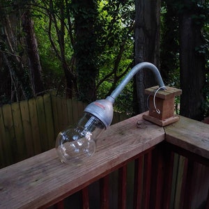 May include: A silver outdoor light fixture with a clear glass globe, mounted on a wooden deck railing.