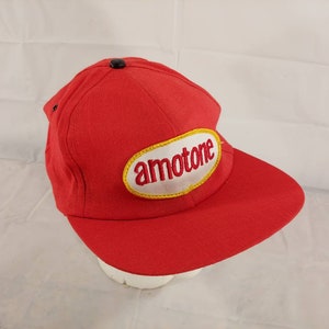 Puede incluir: Gorra de béisbol roja con un parche ovalado blanco que dice "amotone" en letras amarillas.