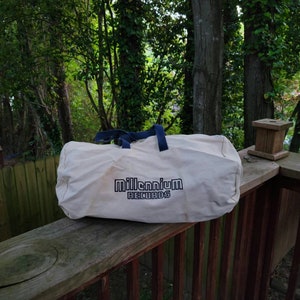 Peut inclure: Un sac de voyage en toile blanche avec des poignées bleues et le texte "Millennium Records" imprimé sur le devant.