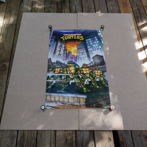 May include: A Teenage Mutant Ninja Turtles poster featuring the four turtles in a fighting stance against a cityscape backdrop. The poster has a purple background with the words "Teenage Mutant Ninja Turtles" and "Turtles" in white.