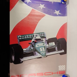 May include: A green and white Porsche race car with the number 8 on the side. The car is driving on a track with an American flag in the background. The text "Quaker State" and "Porsche" are visible on the car. The year 1988 is printed on the poster.