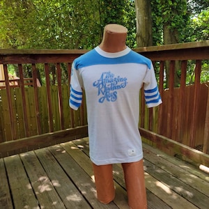 May include: White t-shirt with blue and white striped sleeves. The shirt has a blue graphic that says "The Amazing Rhythm Aces".