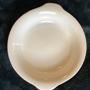 May include: White ceramic baking dish with a rounded shape and slightly flared edges. The dish is empty and has a smooth, glossy finish.