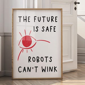 May include: A framed art print with the text "THE FUTURE IS SAFE ROBOTS CAN'T WINK". The artwork features a red eye illustration with radiating lines. The frame is made of light brown wood.