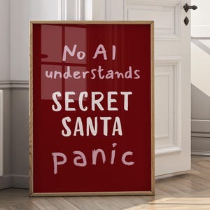Pode incluir: Uma impressão vermelha emoldurada com texto branco que diz "No AI understands SECRET SANTA panic". A moldura de madeira envolve a impressão, que está encostada em uma porta branca e em um chão de madeira.