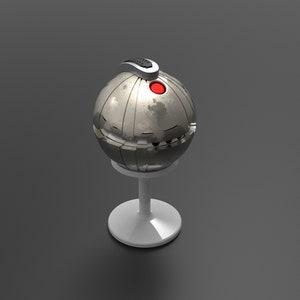 May include: A silver sphere with a red button and a black handle sits on a white pedestal. The sphere has a textured surface and appears to be made of metal.