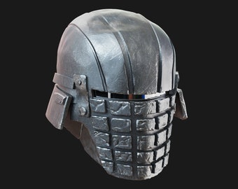 Könnte beinhalten: Ein silberner Helm mit einer Gesichtsmaske aus kleinen, quadratischen Platten. Der Helm hat ein Visier und einen Kinnriemen.