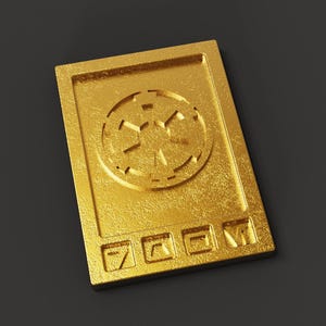 Puede incluir: Un dispositivo de metal de color dorado con un diseño circular y cuatro botones. El dispositivo tiene una superficie texturizada y un diseño en relieve.