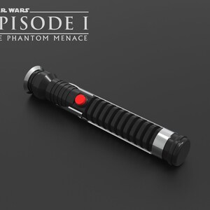 May include: A black lightsaber with a silver handle and a red button. The lightsaber is from the Star Wars Episode I: The Phantom Menace movie.