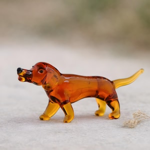 Könnte beinhalten: Kleine Hundefigur aus bernsteinfarbenem Glas. Der Hund ist in einer Laufposition dargestellt, mit erhobenem Schwanz. Die Figur hat eine glänzende Oberfläche und die Details, wie Ohren und Pfoten, sind gut erkennbar. Der Hintergrund ist neutral.