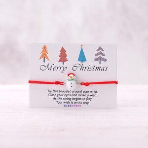 May include: Red string bracelet with a snowman charm. The card reads "Merry Christmas" and includes instructions to tie the bracelet around your wrist, close your eyes, make a wish, and as the string frays, your wish will come true. The card is signed "GLASSTUFF".