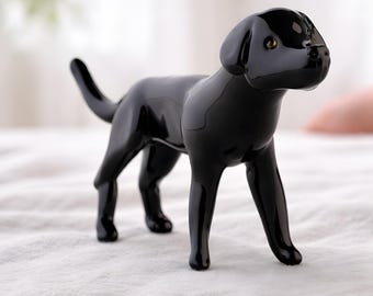 May include: A glossy black Labrador dog figurine. The dog is standing on all fours with its tail up. The figurine has a smooth, reflective surface and small, yellow eyes. The dog is a decorative item.