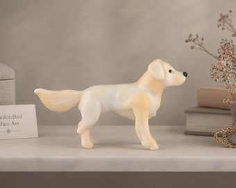 May include: A handcrafted glass dog figurine, predominantly white with pale yellow highlights. The dog is depicted in a standing position. The figurine is displayed on a white surface against a neutral backdrop. A sign reads "Handcrafted Glass Art."