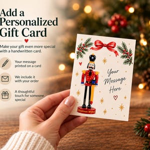Gift card of the Nutcracker's long black glass legs and shoes, standing securely on the round red display base.