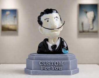 May include: A glass bust of a man with a distinctive moustache and slicked-back hair, wearing a black suit and a white shirt. The bust sits on a grey pedestal with the words "CUSTOM For You" engraved. A small blue object is on the right side.
