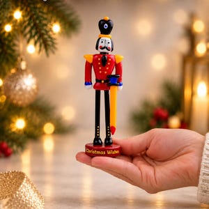 Front view of a colorful lampworked glass Nutcracker soldier with a black hat, red uniform, black boots, and a red display base.