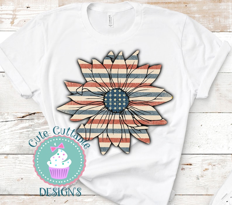 Op de afbeelding: Wit T-shirt met een rood, wit en blauw zonnebloemontwerp. De zonnebloem is gemaakt van de Amerikaanse vlag. De tekst "Cute Cuttable Designs" staat in een cirkel onder de zonnebloem.