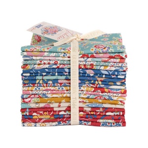 May include: A stack of patterned fabric squares in various colors, including blue, red, and yellow, tied with a cream ribbon. A tag with floral illustrations is attached. The fabric appears to be cotton, suitable for quilting or crafting projects.